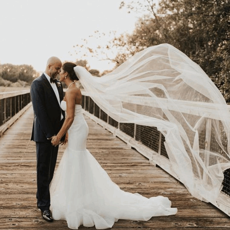 Bride and groom holding hands on a wooden bridge, bride’s veil flowing in the wind, groom in a tailored navy tuxedo.