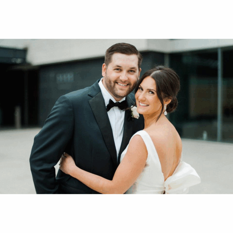 Bride and groom embracing on their wedding day; groom in a classic black tuxedo with satin lapel, bride in a white gown with statement bow. Wedding at Orchestra Hall.