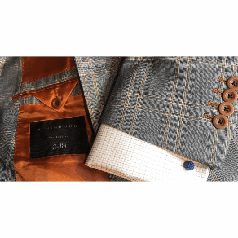 Close-up of a custom J.Hilburn blazer featuring orange satin lining, personalized label, plaid pattern, stacked buttons, and a dress shirt with navy cufflink.