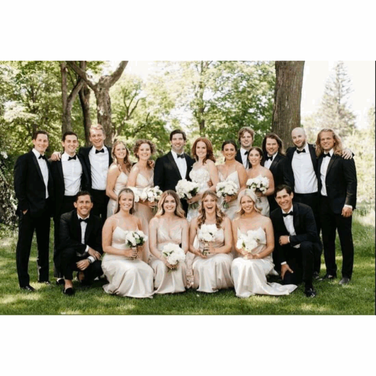 Outdoor wedding photo featuring a full bridal party; groomsmen in classic black tuxedos and bridesmaids in matching champagne satin dresses.