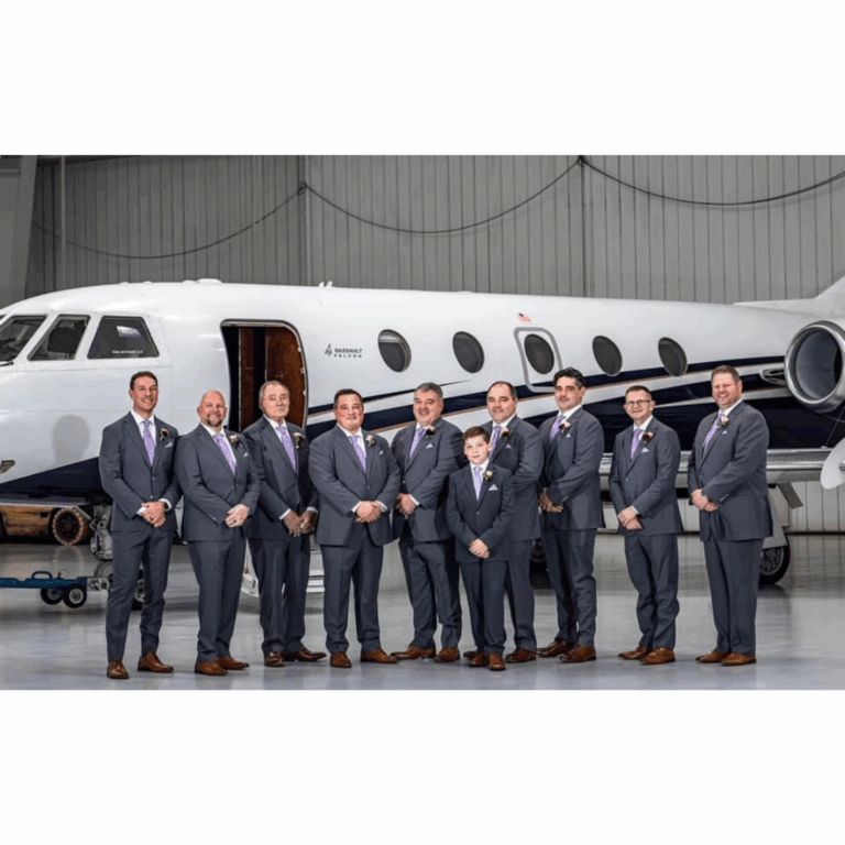 Groom and groomsmen in matching custom gray suits with lavender ties, standing in front of a private jet in a hangar. Flying Cloud Airport Eden Prairie Minnesota